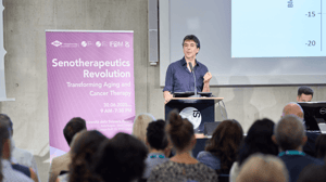 Professor Valter Longo speaks at the Senotherapeutics Revolution forum, addressing an attentive audience alongside the official event banner.