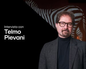 Ritratto di Telmo Pievani accanto al testo “Intervista con Telmo Pievani – Nomadic, Canto per la biodiversità.” Indossa una giacca grigia e un dolcevita nero, su uno sfondo scuro con un motivo stilizzato di zebra. Il logo di IBSA Foundation for scientific research appare in basso.