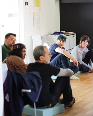 Participants seated on blue cushions in a bright room, during a moment of listening and discussion at Casa Carlo Cattaneo, Switzerland.