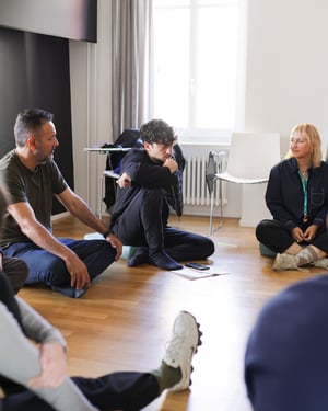 Participants sitting in a circle on cushions during a moment of dialogue and reflection; in the center, notes and a smartphone resting on the floor.
