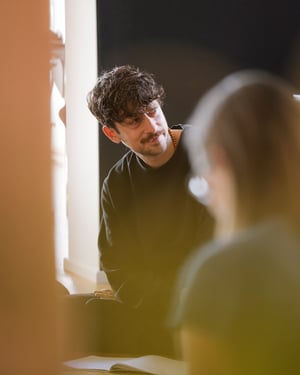 Close-up of a man sitting on the ground listening attentively to another person off-camera during a workshop or group meeting.