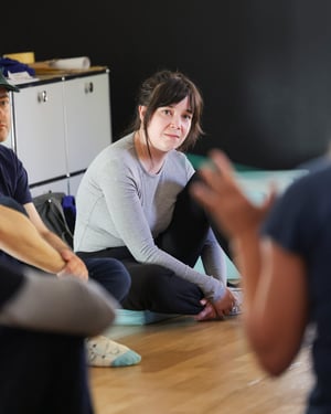 Woman sitting on the floor listening attentively to a speech during a group meeting in a bright space.