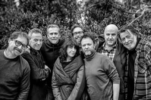 Black and white group photo of the full cast and staff of the Nomadic show by Telmo Pievani and Gianni Maroccolo, standing close together outdoors.